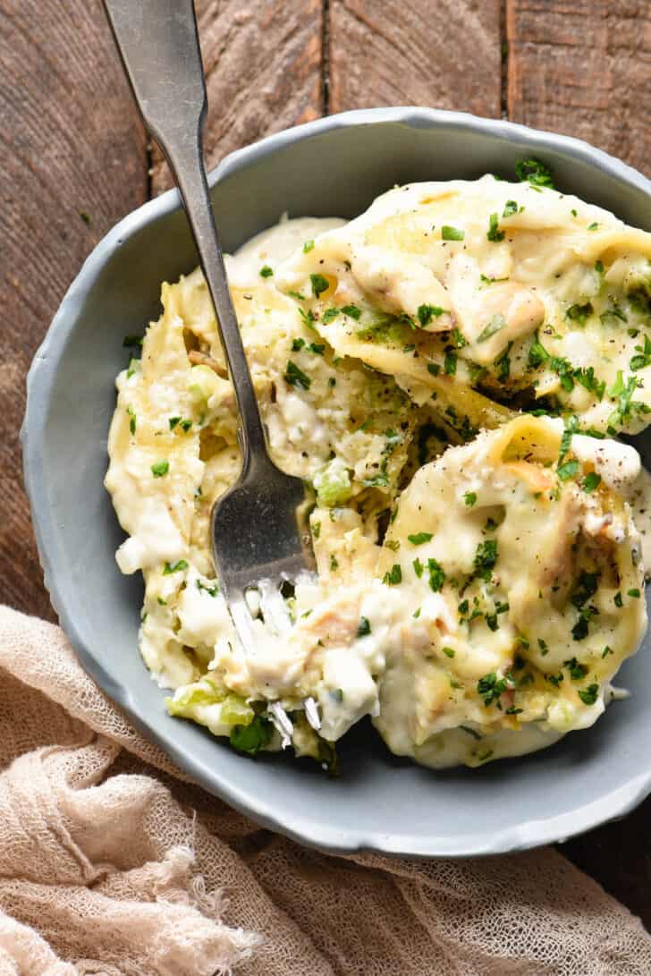 A closeup on a chicken alfredo stuffed shells recipe, in a gray bowl with a fork digging in.