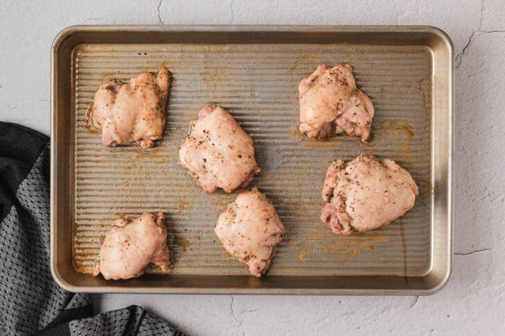 Six cooked chicken thighs on a rimmed baking pan.