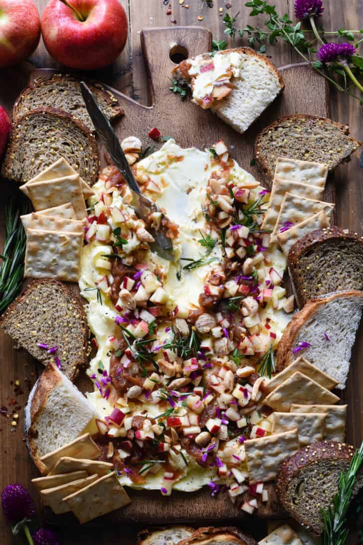 An autumn appetizer spread made with apple puree, fresh apples, nuts and herbs on a wooden platter, with bread and crackers for dipping.