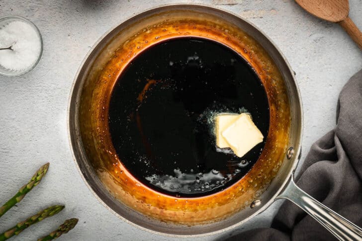 A dark brown reduction being made in a pan, with two pats of butter added to it.