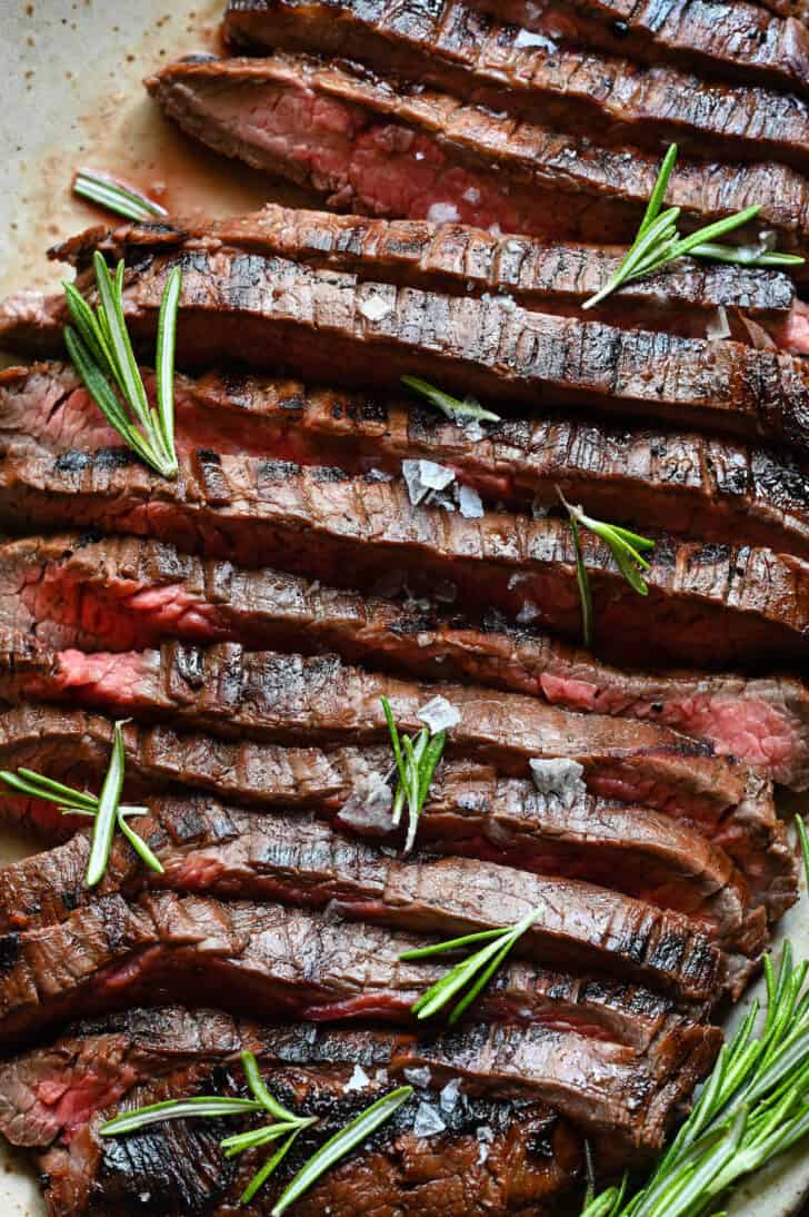 A cooked, sliced slab of beef on a speckled platter, with rosemary garnish.