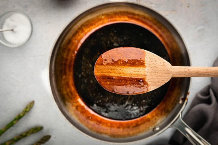 A wooden spoon coated in balsamic vinegar reduction with a line swiped through it.