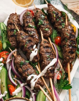 A large platter filled with kafta skewers, vegetables and a creamy dipping sauce.