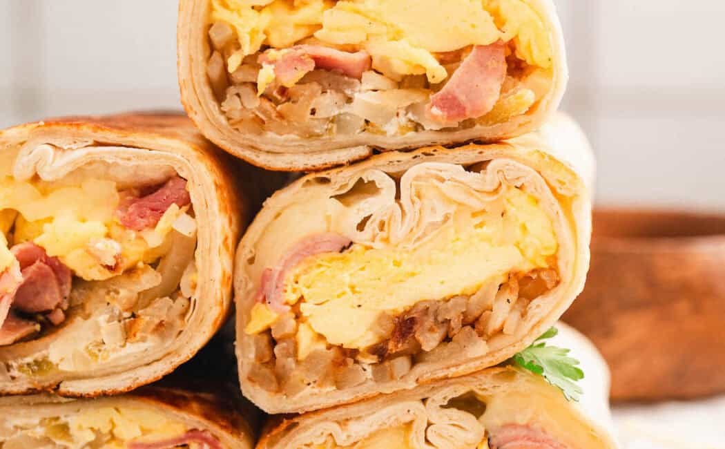 A stack of the best breakfast burritos in front of a light tile background.