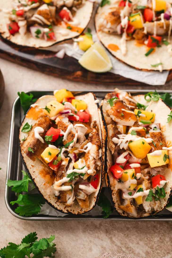 The best fish tacos topped with tropical fruit salsa and drizzled with creamy sauce.