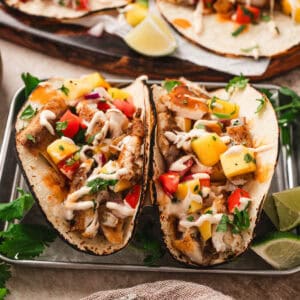 A fish taco topped with tropical fruit salsa and drizzled with creamy sauce.