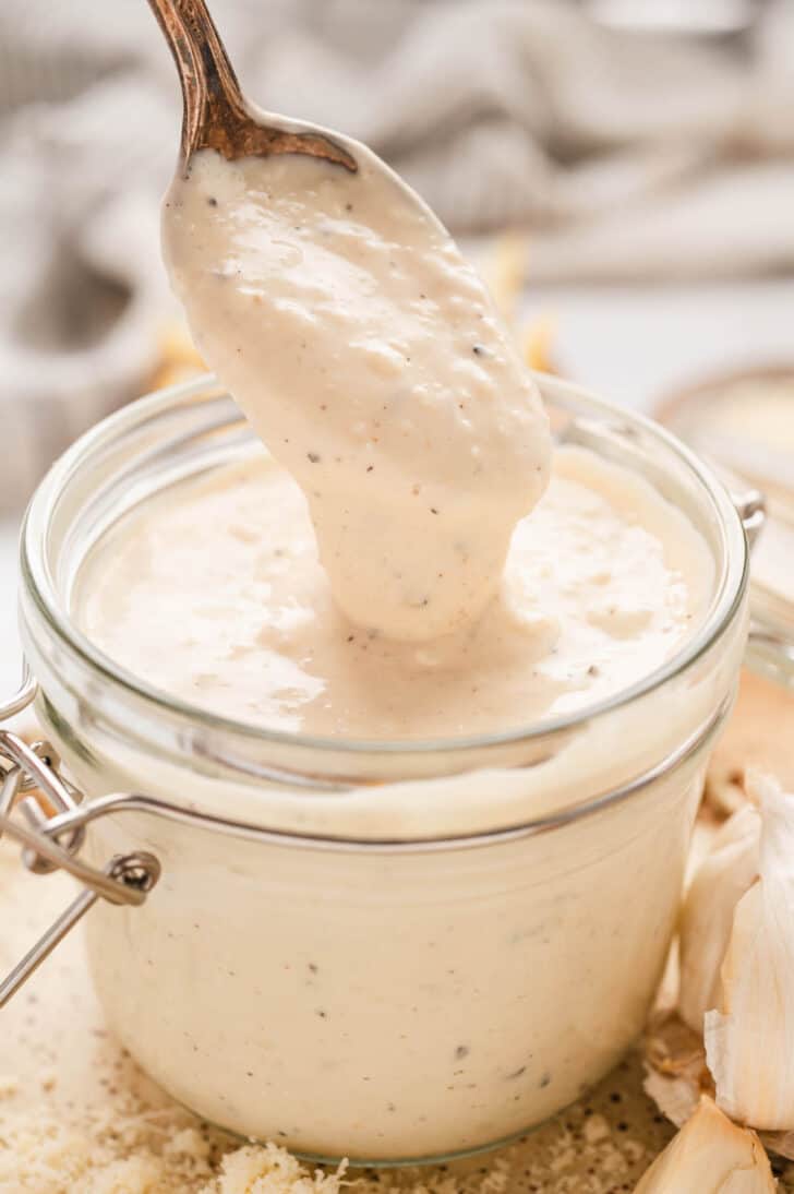 A glass jar filled with a creamy sauce mixture, with a spoon lifting some out.