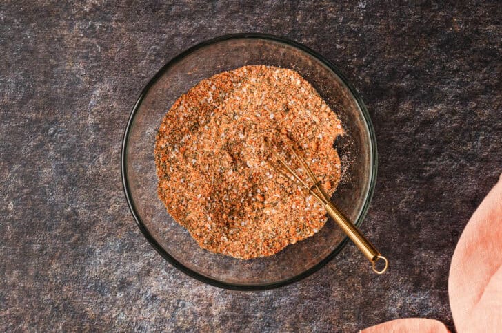 A glass bowl with a whisk stirring together a spice rub.