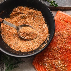 A black bowl filled with seasoning for salmon with a spoon in it.