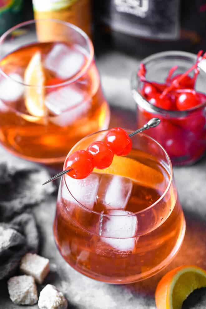 Two brandy old fashioneds garnished with maraschiono cherries and orange slices.