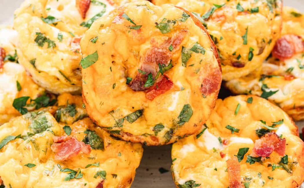 A white plate topped with breakfast muffins made with eggs, bacon, veggies, cheese and herbs.