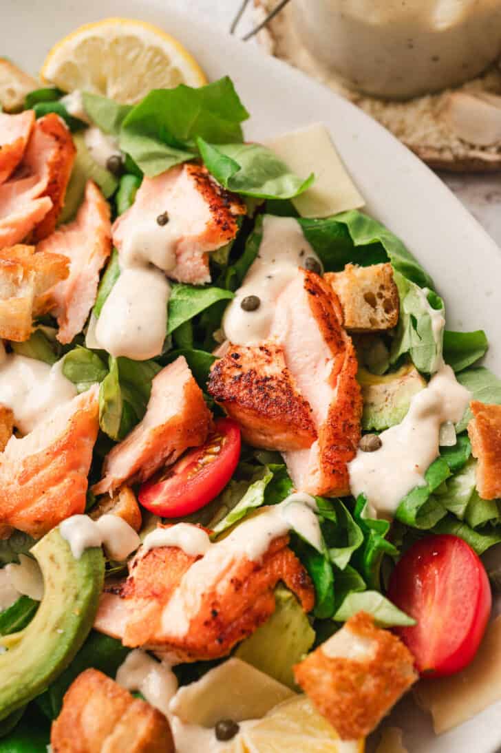 A salad made with lettuce, tomato, avocado, cooked salmon, capers and a homemade caesar salad dressing recipe.