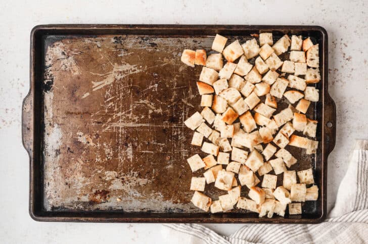 A rimmed baking pan where half is filled with bread cubes.