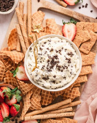 A bowl of cannoli dip on a platter with waffle pieces, graham crackers and strawberries.