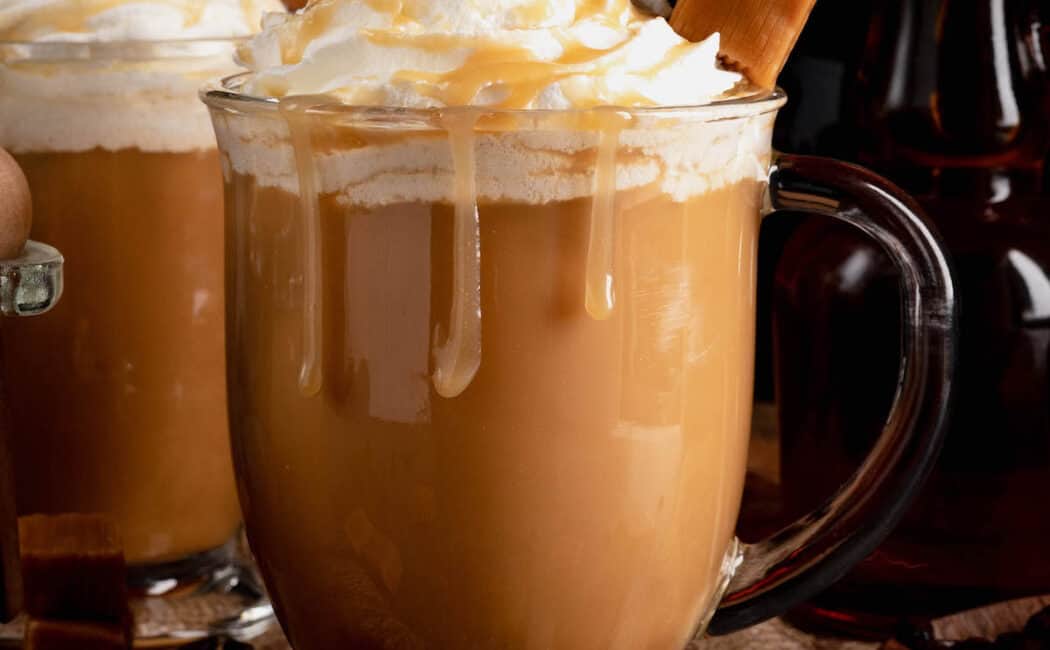 A glass mug filled wth creamy caramel coffee and garnished with whipped cream and a skewer of caramel candies.