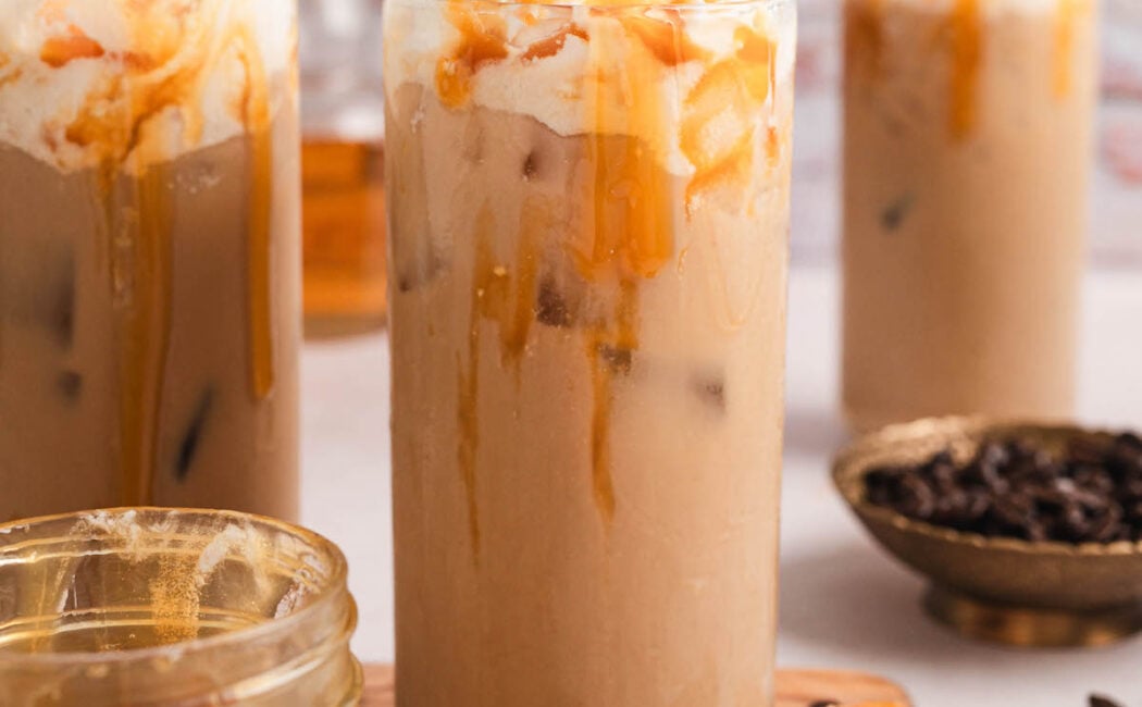 A tall glass of caramel iced coffee in front of a textured brick wall.