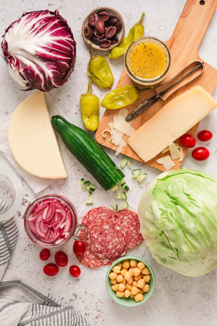 Ingredients on a light background, including radicchio, lettuce, Provolone, salami, tomatoes, chickpeas, cucumber, onion, Parmesan, pepperoncini and olives.