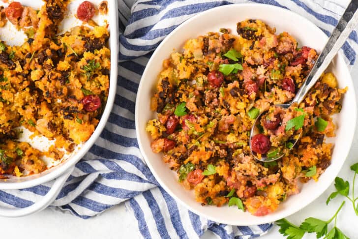 A white bowl filled with chorizo cornbread stuffing made with tart cherries, with a blue and white napkin alongside the bowl.