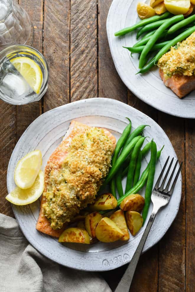 Rustic white plates topped with stuffed salmon with crabmeat, green beans and roasted potato wedges.