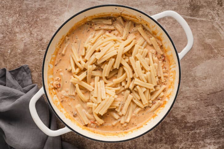 A white Dutch oven filled with a creamy orange sauce, with cooked casarecce pasta on top.