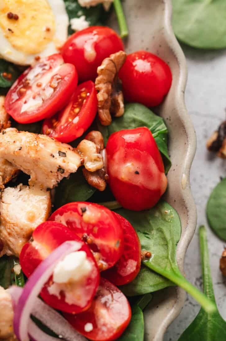 Closeup on a spinach and tomato salad drizzled with the best honey mustard dressing.