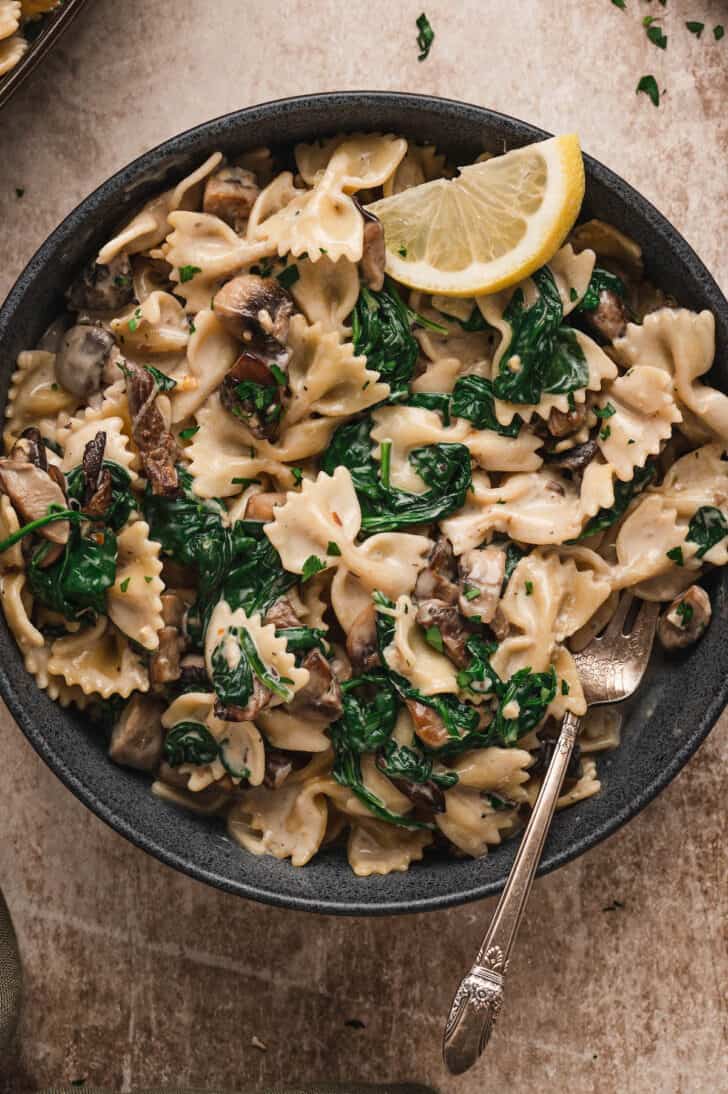 A dark bowl filled with creamy spinach mushroom pasta.