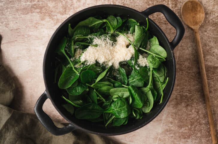 A dark dutch oven filled with spinach and parmesan cheese.