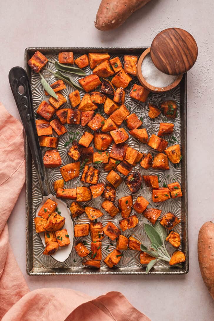 Cubed sweet potatoes in oven on a serving spoon on a textured baking pan.