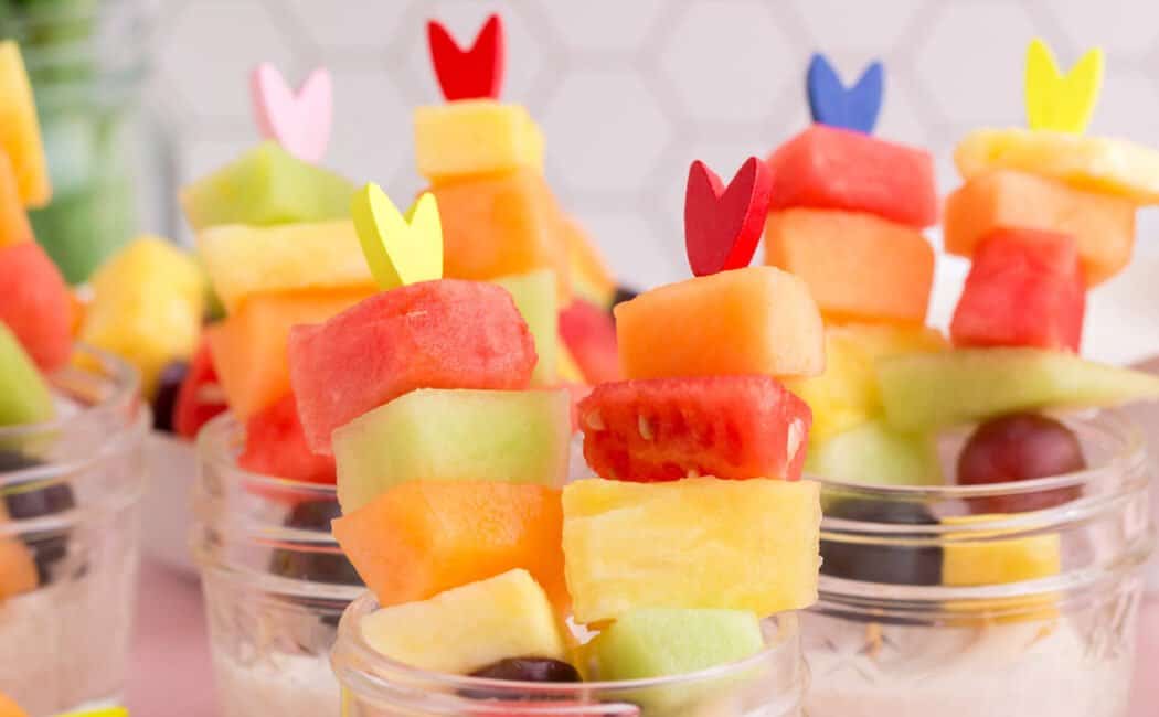 Easter fruit salad, served as half pint mason jars filled with sweet yogurt dip and fresh fruit on fancy toothpicks.