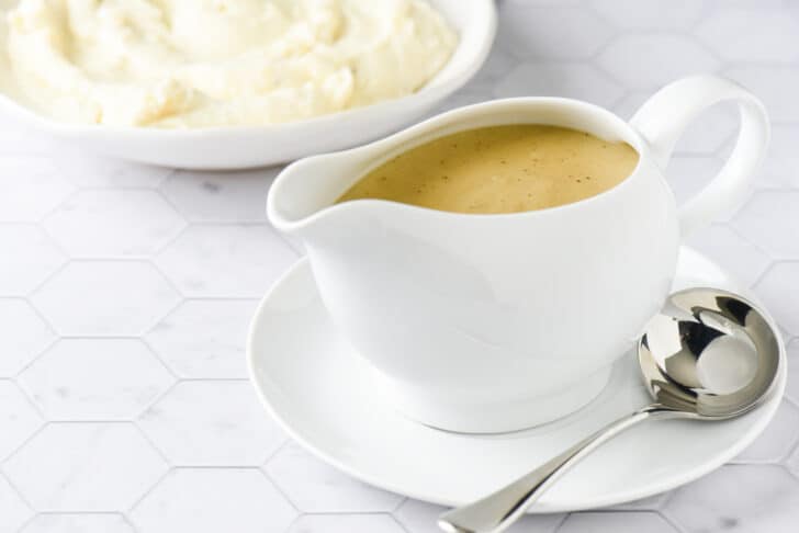 White ceramic gravy boat filled with an easy gravy recipe, with bowl of mashed potatoes in background.