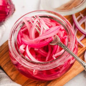 A glass jar filled with quick pickled red onions, with a fork lifting some out.