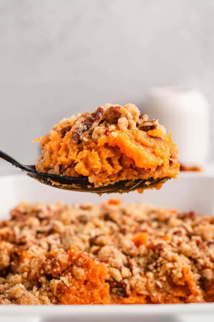 A black spoon lifting a scoop of easy sweet potato casserole from a baking dish.