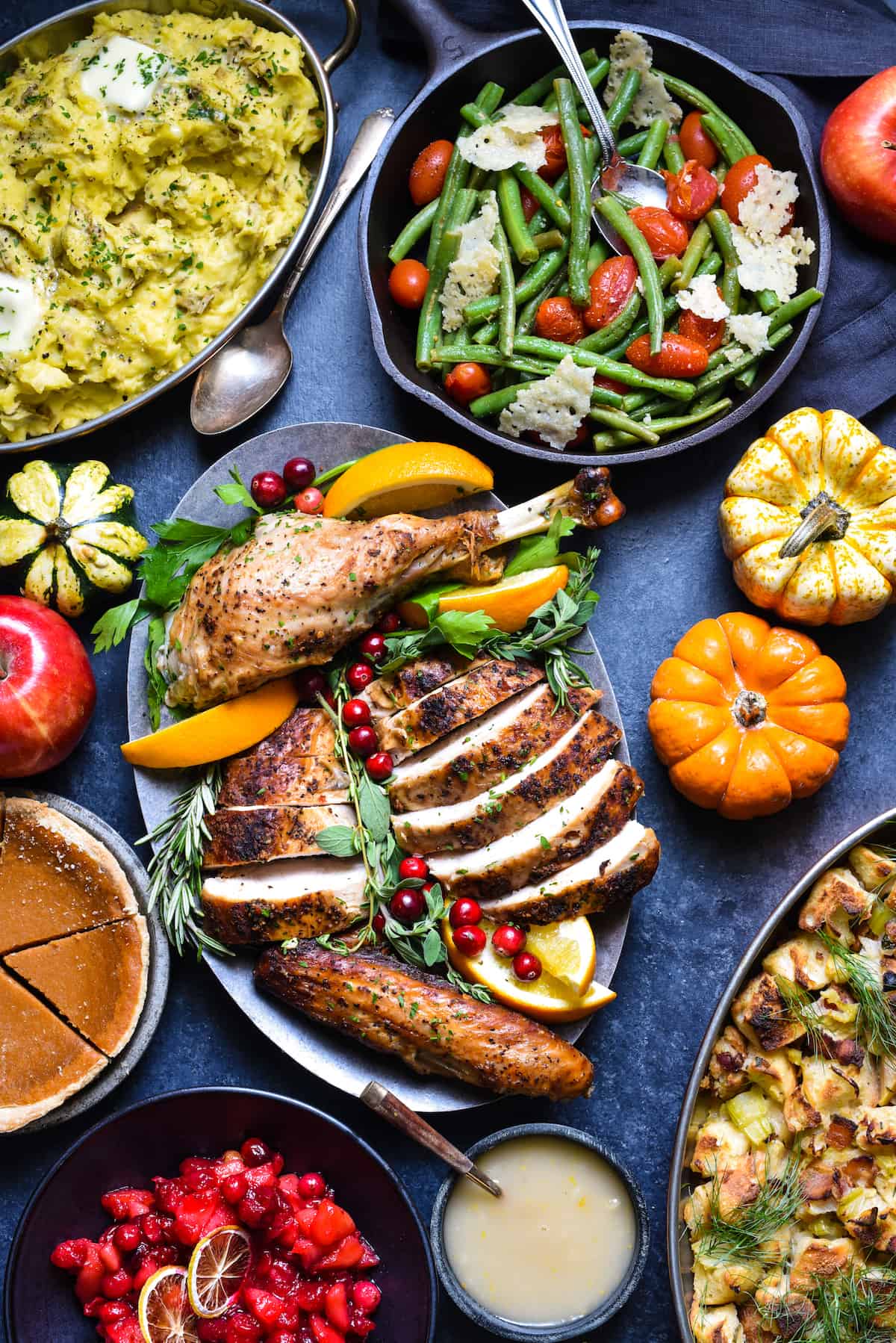 Blue tabletop covered with Thankgiving recipes like roasted turkey, green beans, stuffing, mashed potatoes and cranberry sauce.