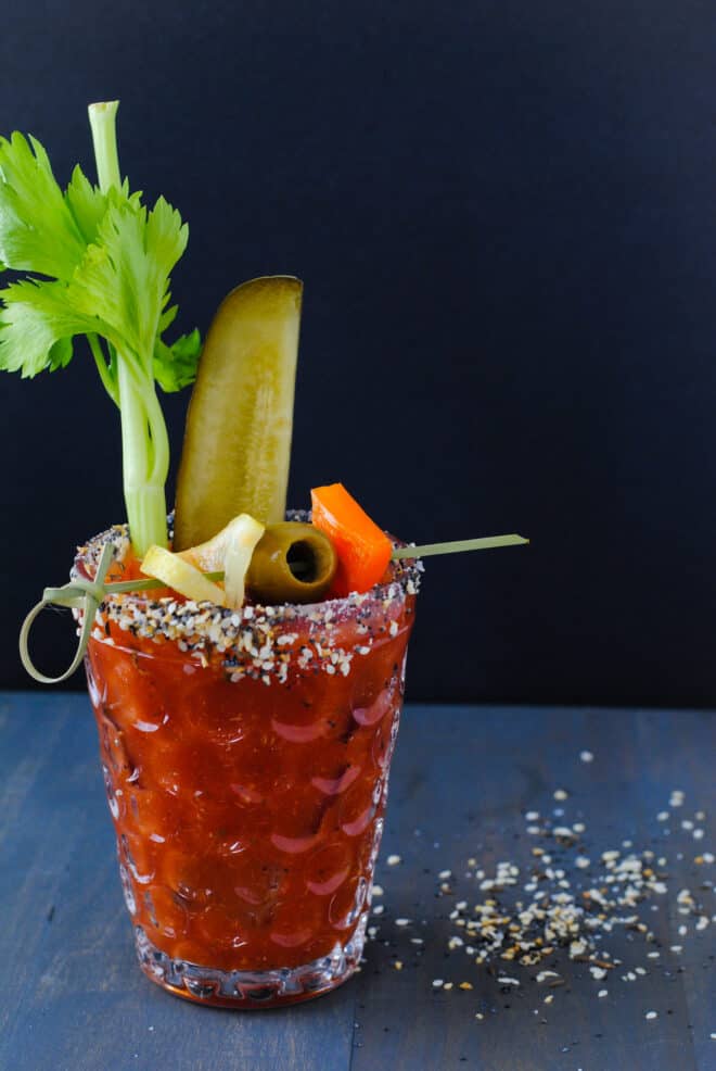 Large glass rimmed with bloody mary rim salt and filled with homemade bloody mary mix and garnishes like celery, pickles and olives.