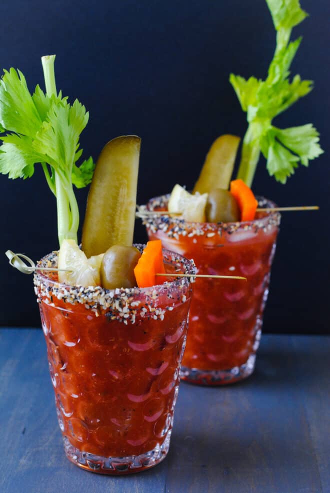 Two glasses rimmed with seeds and spices and filled with homemade bloody mix and lots of garnishes.