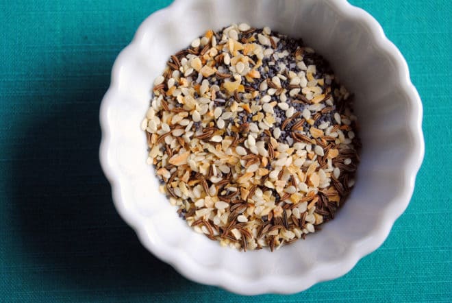 Small white bowl on teal background, filled with everything bagel seasoning mix.