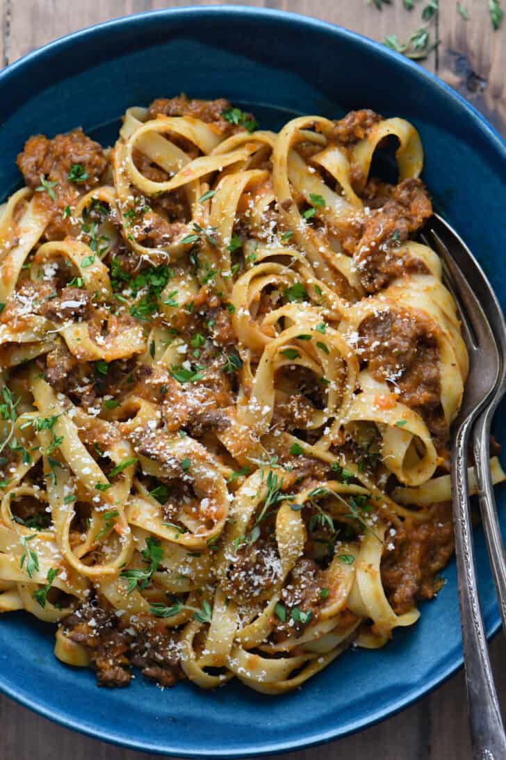 A blue bowl filled with pasta and meat sauce, garnished with herbs and Parmesan cheese.