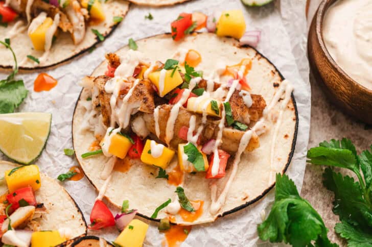 Grilled fish tacos topped with fruit salsa and drizzled with creamy sauce.