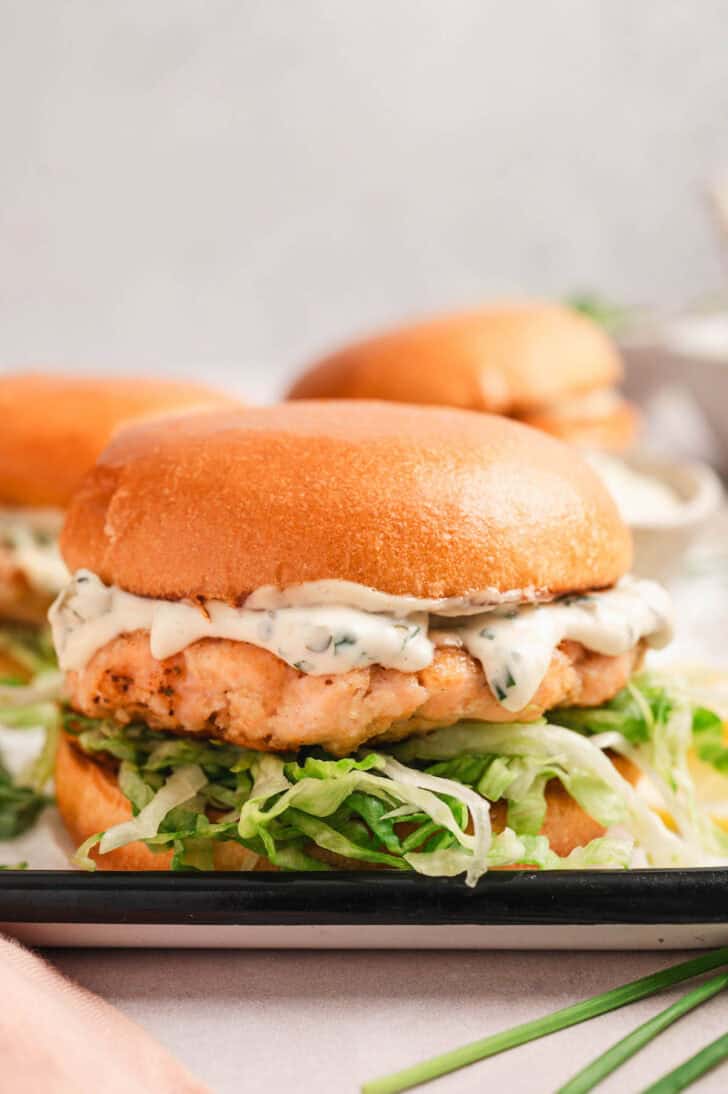 Closeup on a salmon burger recipe topped with tartar sauce and lettuce.