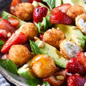 A large platter filled with fried goat cheese balls, strawberries, avocado, pine nuts and basil.