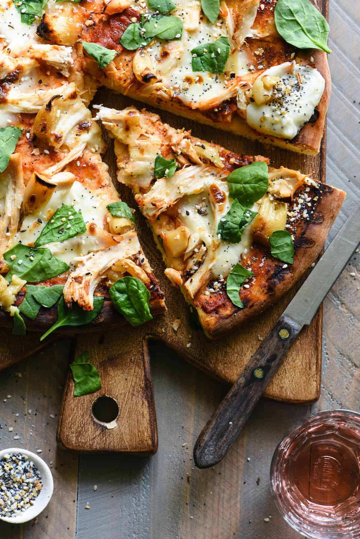 Overhead photo of cut chicken pizza on cutting board with knife.