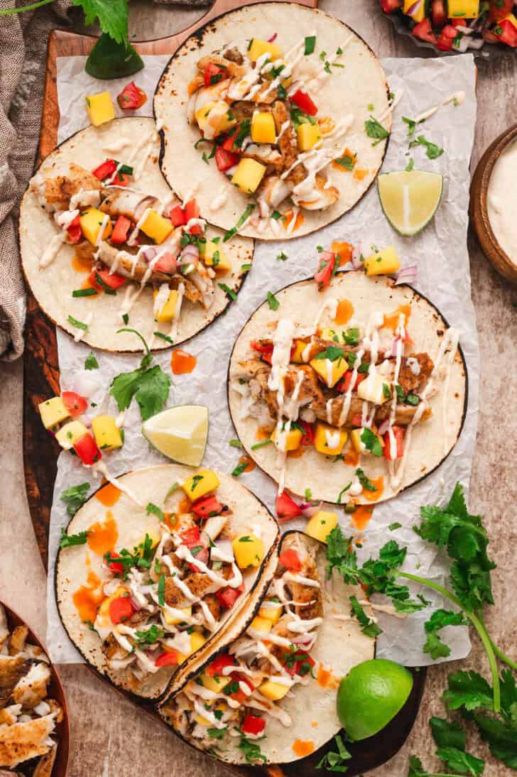 A recipe for fish tacos topped with fruit salsa and drizzled with creamy sauce.