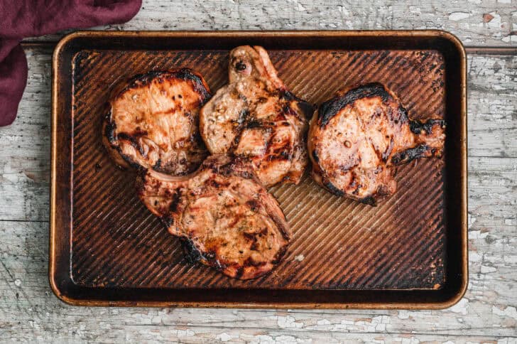 Grilled pork chops on a textured baking pan.