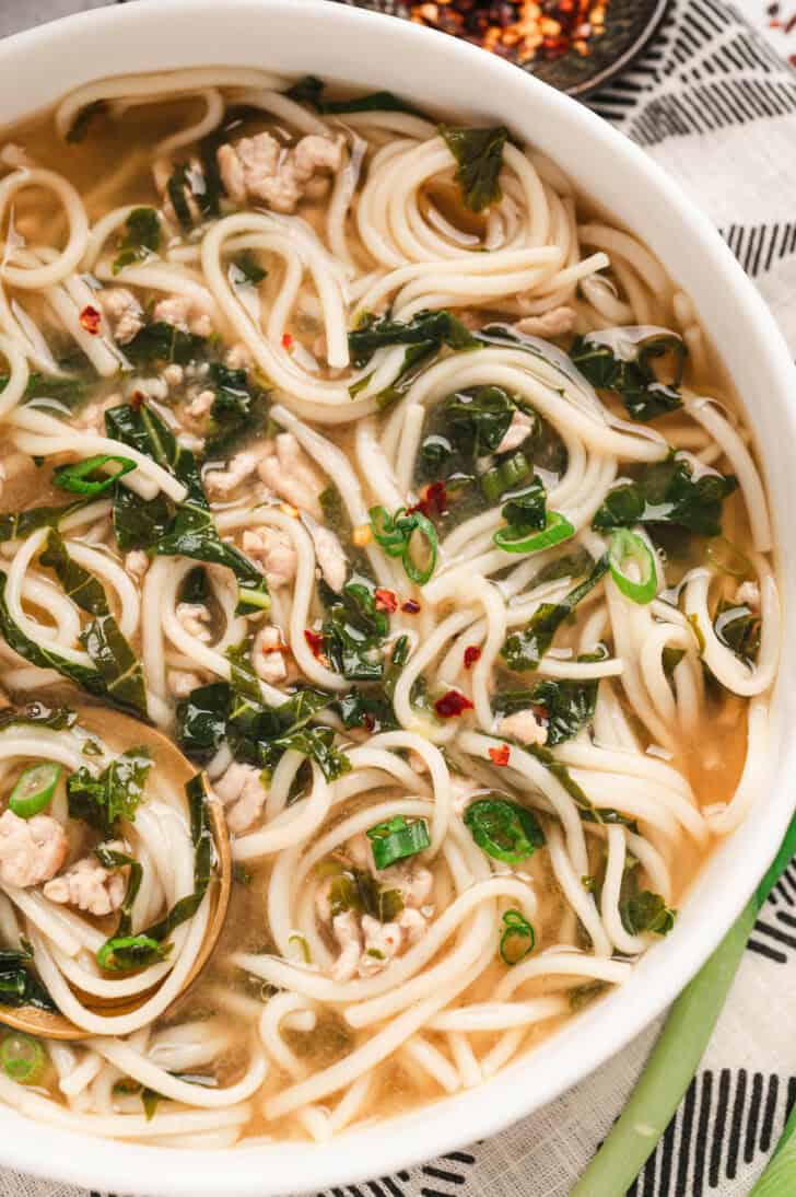 A shallow white bowl filled with pork soup with noodles.