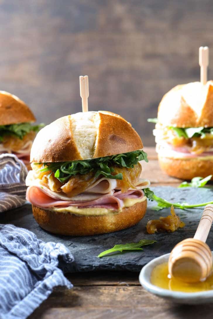 Pretzel bun sliders made with turkey, ham, arugula, mustard and caramelized onions on a slate platter.