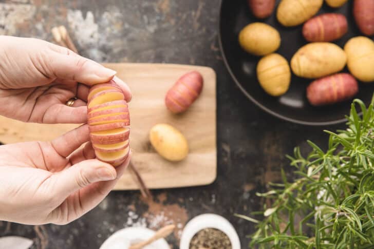 Two hands showing a potato that has been cut hasselback style.