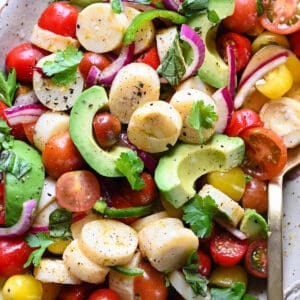 A speckled oval platter filled with hearts of palm salad made with tomatoes and avocado.