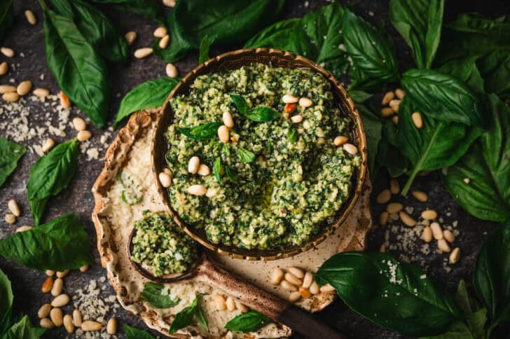 A bowl of a homemade pesto recipe garnished with pine nuts and fresh basil.