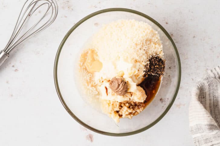 A glass bowl filled with mayonnaise, grated cheese, Dijon mustard, anchovy paste, garlic, spices and Worcestershire sauce.