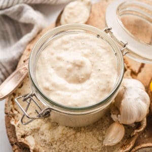 A lidded glass jar filled with the best homemade Caesar dressing, surrounded by the ingredients for the dressing.